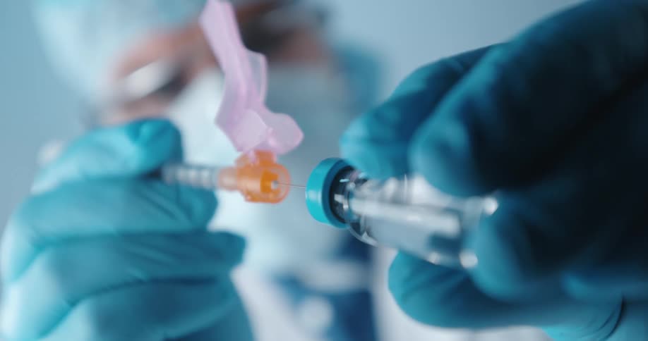 A doctor or nurse fills a syringe from a small medicine bottle then extracts the needle