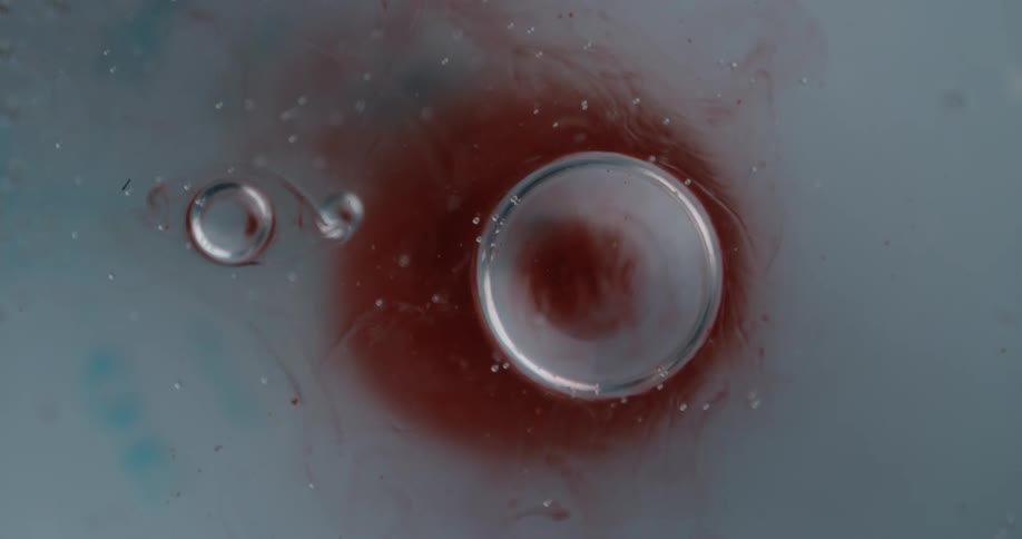 Bright red liquid ink flowing around air bubbles in a pool of water