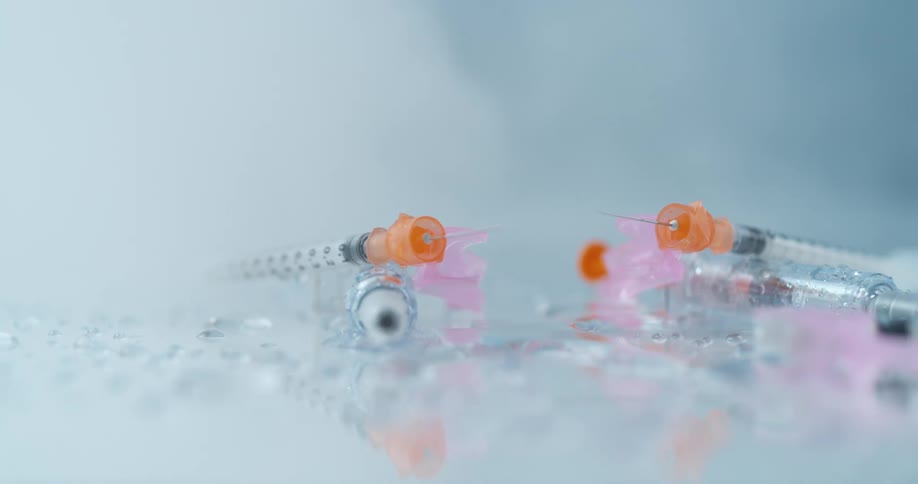 Syringes and needles lying on a mirror with broken glass