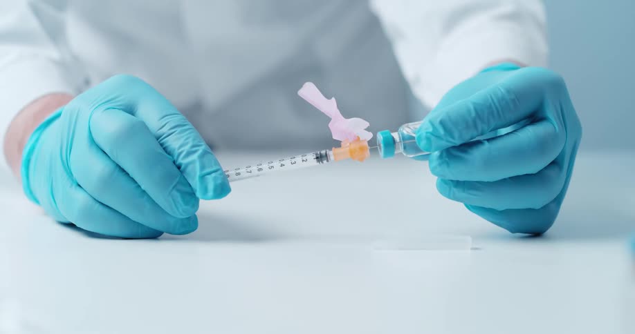 Close up of a syringe being filled with medication with blue gloved hands