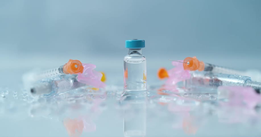 A medicine vial on a reflective surface with melting ice and syringes
