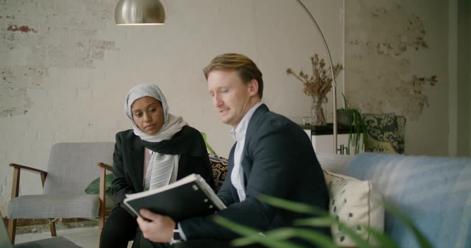 A man gestures and points to a laptop while in a business meeting with a woman