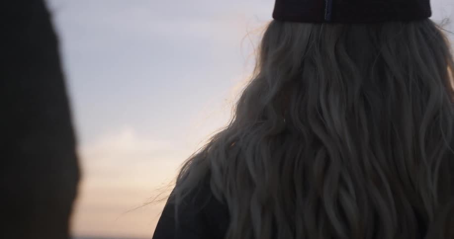 A woman with blonde hair watches a sunset