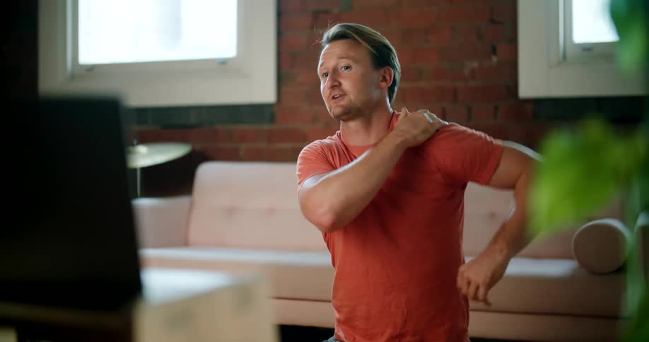 A man stretching his shoulder on the floor in front of a sofa