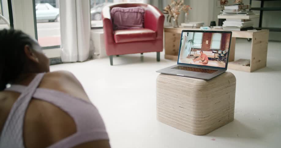A woman does yoga while using a laptop to participate in a video chat with a man who is also doing yoga