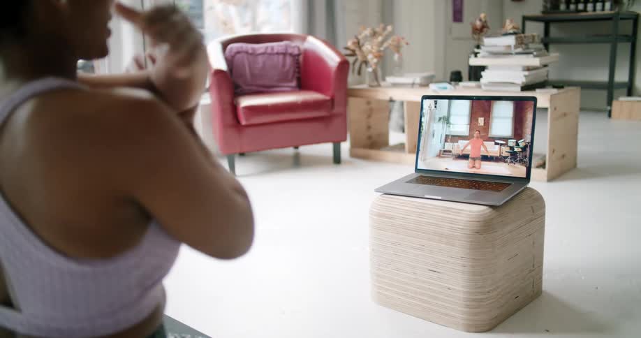 A woman practices yoga while using a laptop to participate in a video conference with a man who is also practicing yoga