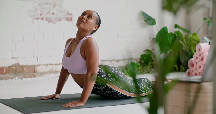 A woman arches her back as she demonstrates a yoga pose in front of an open laptop computer