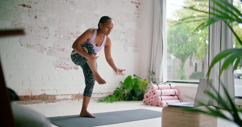 A woman in a sports bra balancing on one leg on a yoga mat