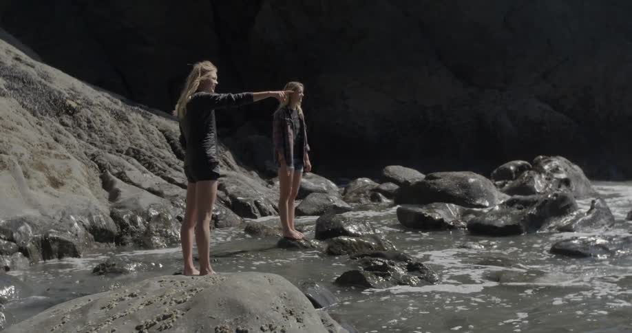 Two women stand on a rocky beach and look towards the ocean