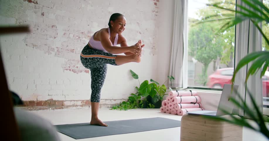 A yoga instructor holds her leg straight out and brings it back in as she live streams her class