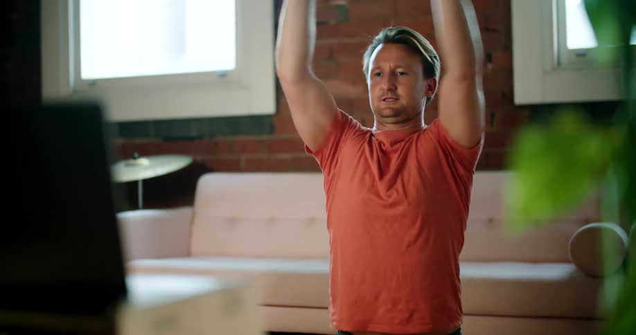Young man stretching in the living room at home doing an online class