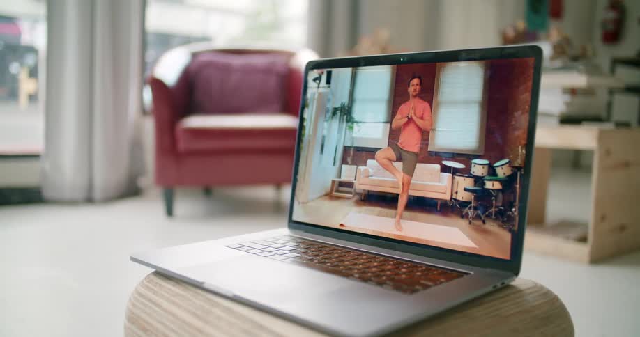 A laptop on a stool in a room with a chair and a window in the background