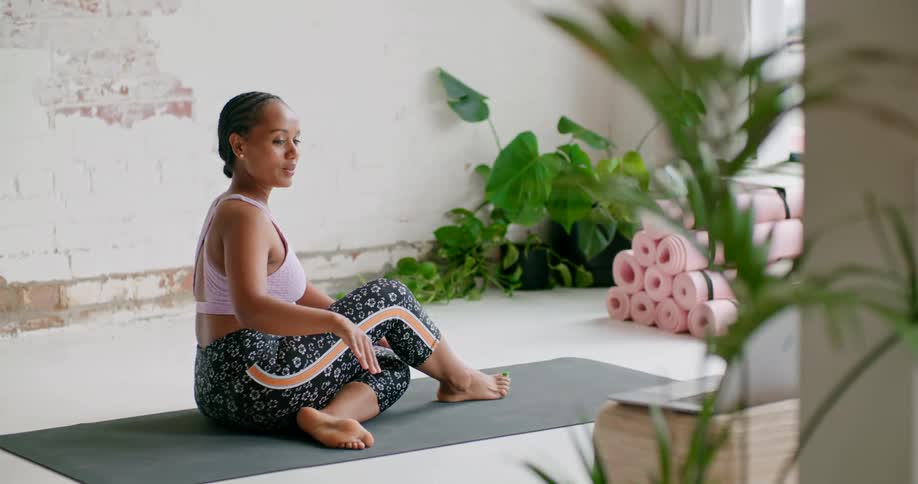 A woman sitting on a yoga mat instructs others via video conferencing about performing a yoga pose