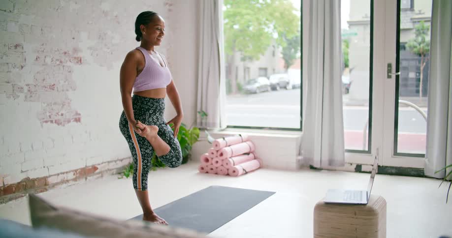 A woman is talking on a video conference as she performs yoga