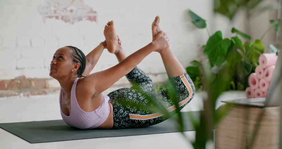 A female yoga instructor stretches her legs behind herself while on her belly in front of a laptop