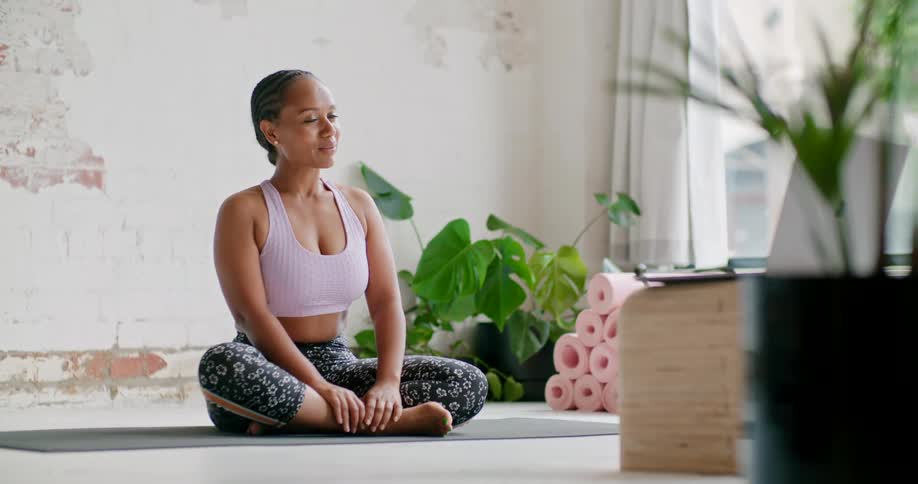 Young fit woman wearing sports clothes sitting on the floor teaching yoga online on a laptop