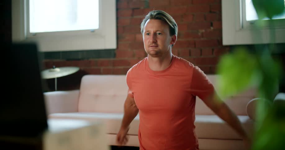 A man in a room stretching with a couch and a wall in the background