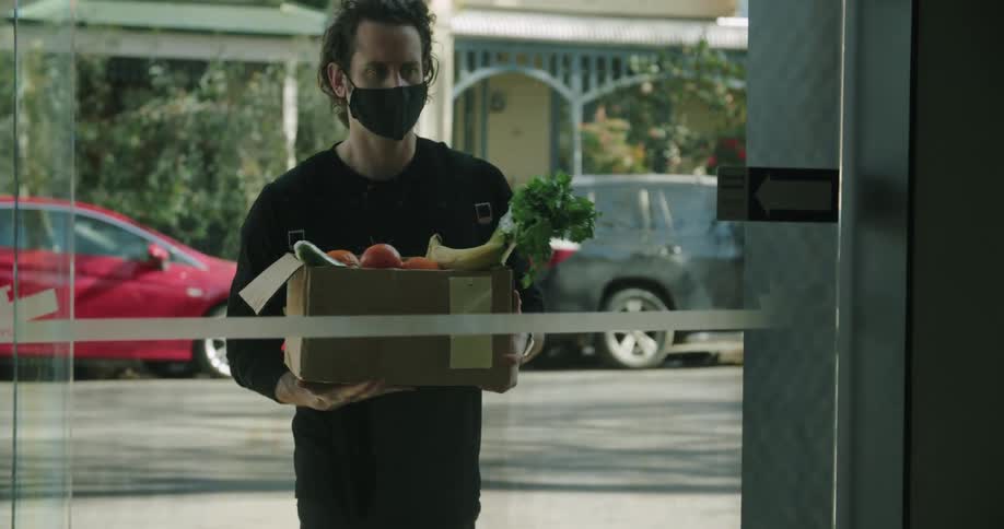 A person is walking into a store with a box of fresh vegetables