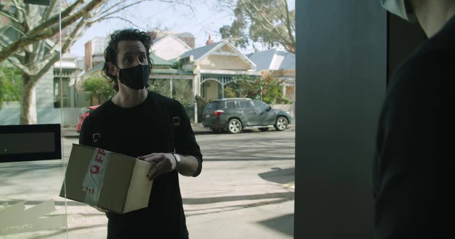 A man wearing a face mask delivering a cardboard box to a customer