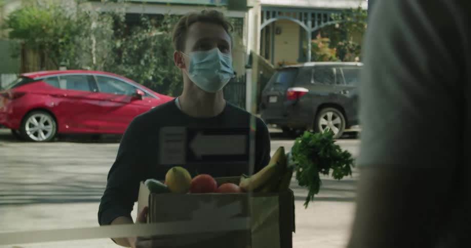 A man receiving a messenger delivering a box of groceries filled with fruit and vegetables