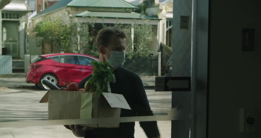 A man delivering groceries looks at his cell phone puts it in his pocket and then rings a doorbell