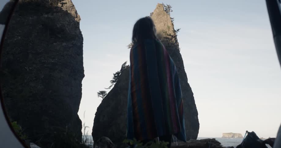 A person wearing a blanket around them is standing in the shadows