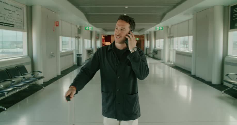 A man talks on his smartphone while pulling luggage through an airport