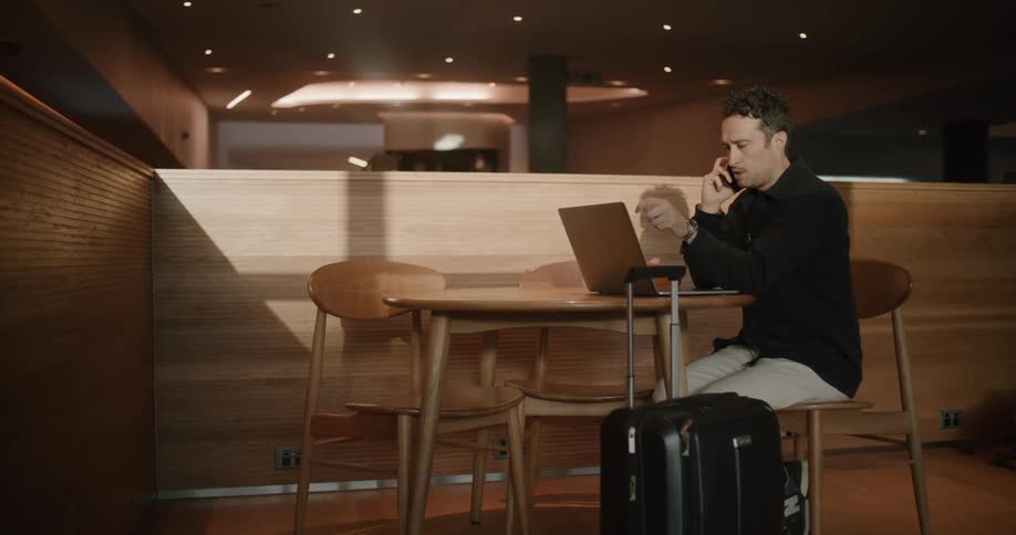 A man talking on the phone and looking at a laptop in an airport