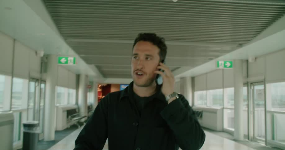 A man walks through an airport terminal with his luggage talking on a cell phone