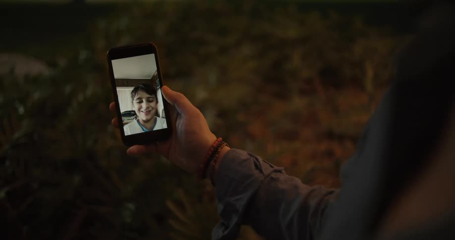 A person receives a video call from a young boy on a smartphone outdoors