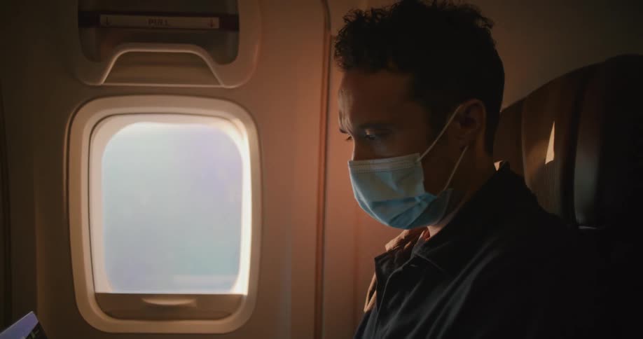 Man wearing a face mask working on a laptop sitting in a plane