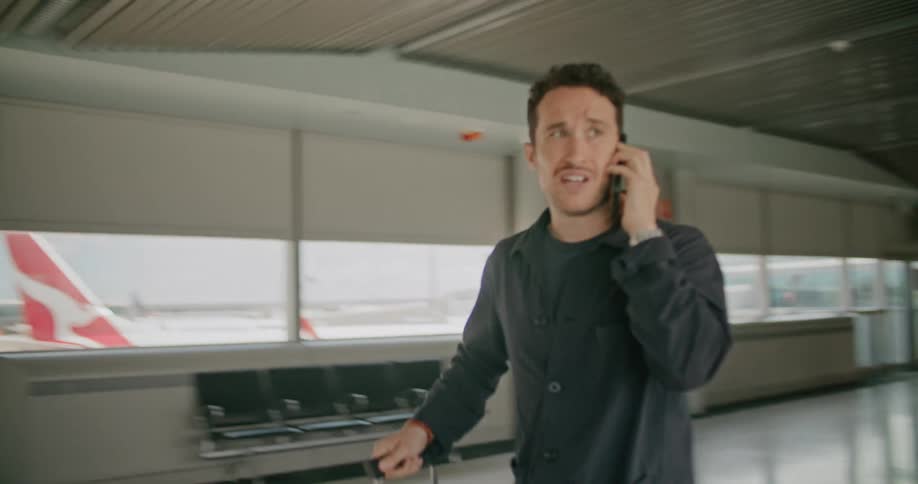 A man that is walking through an airport talking on a phone