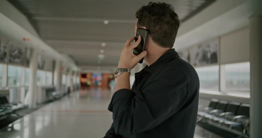 A man standing in the airport looks around confusedly while talking on his smart phone