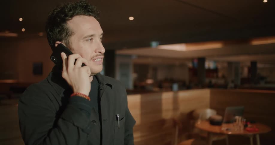 A man stands in a restaurant and talks on a cell phone