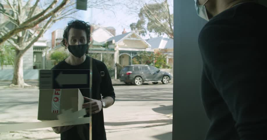 A delivery person goes to a door and hands a box to a man