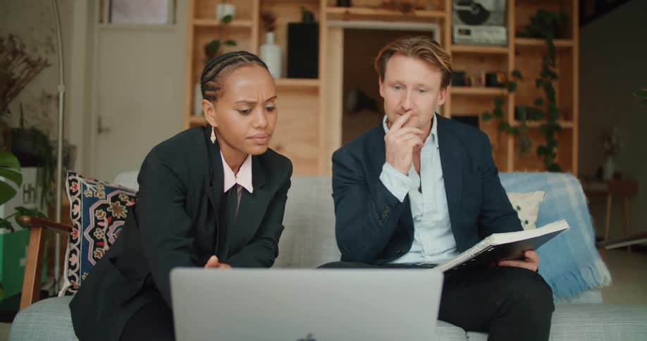 A man gestures at a laptop while talking to a client in her home