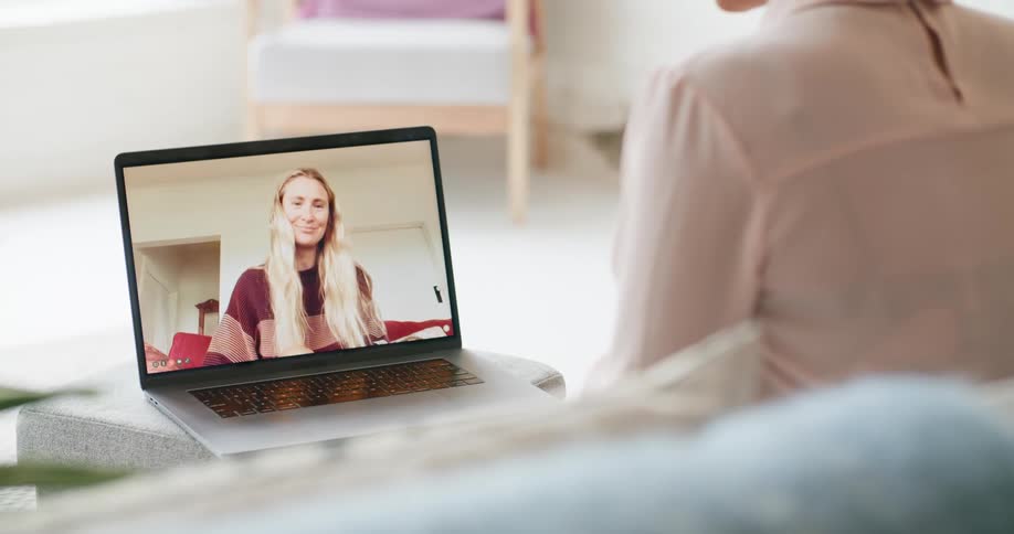 A woman in a room sitting on a couch video chatting on a laptop