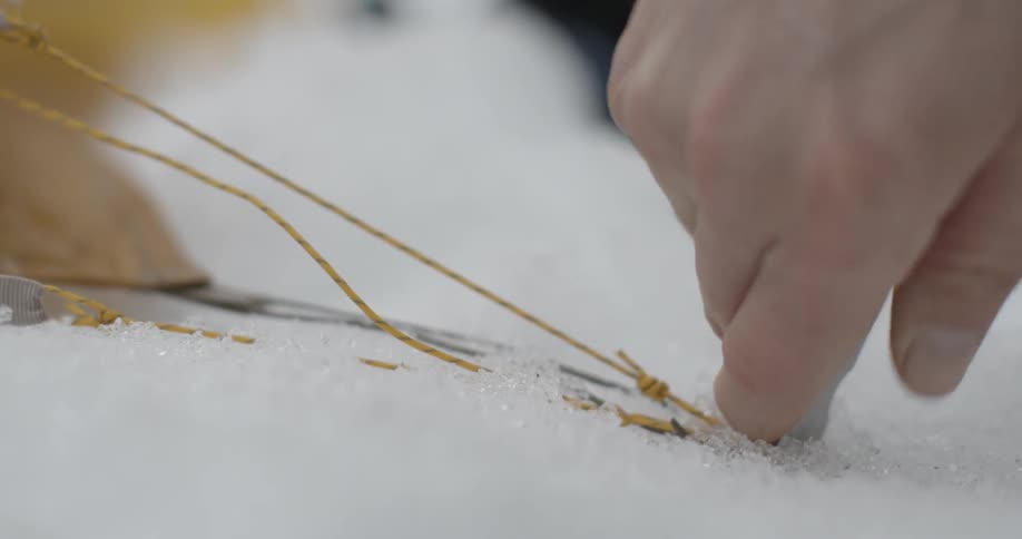 A hand pushes a tent stake into the snow