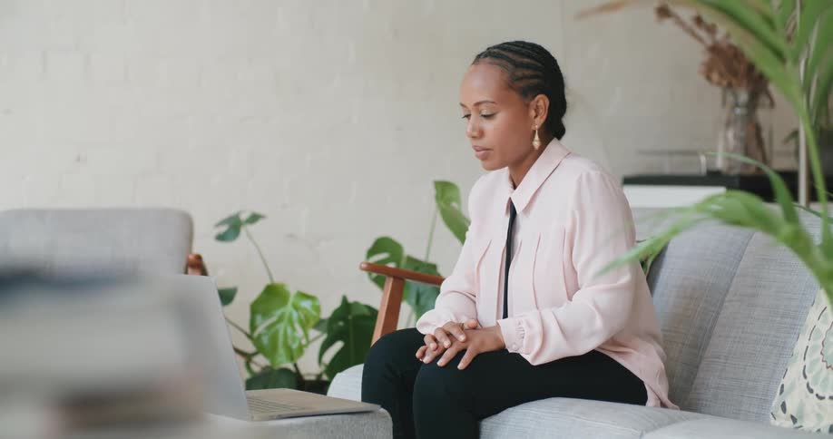 A woman sits on her couch and talks to someone on her laptop while working from home