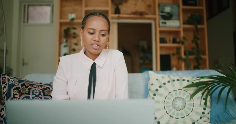 A young woman sits on a couch at home and talks with someone on a laptop