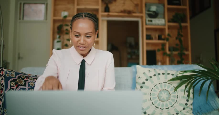 A woman in a tie smiling while video chatting on a laptop in a living room