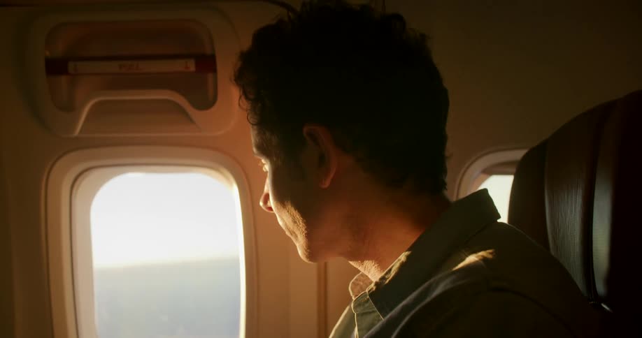 A man sitting on a chair on a plane using a smart phone with windows in the background