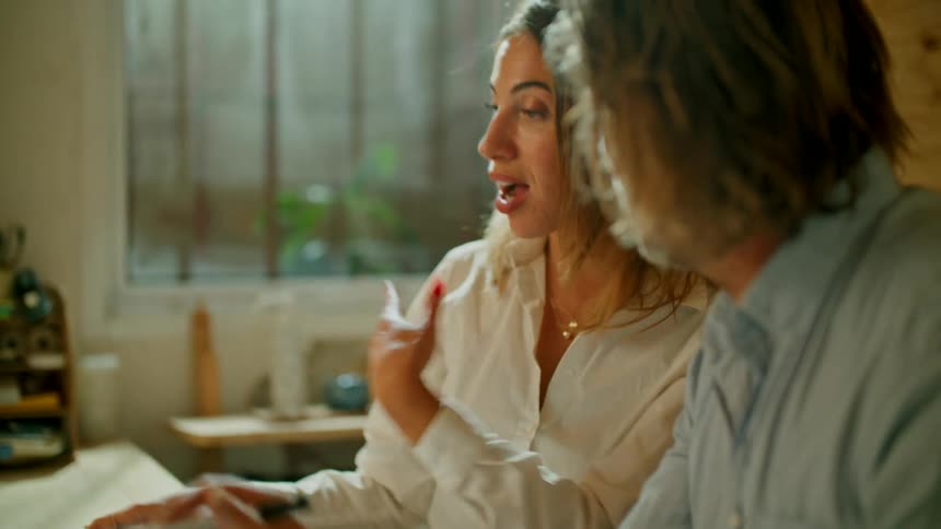 A woman and man sit together at a desk with a laptop talking about what they see on it