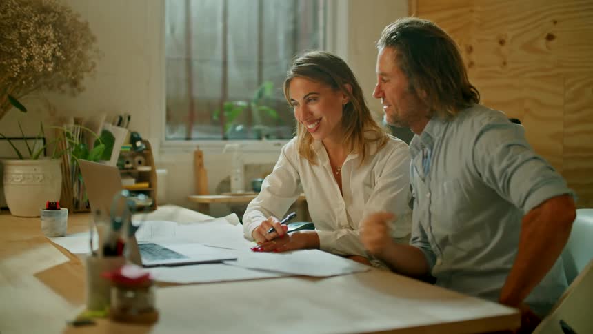 A couple working in an office greeting someone on a video call on a laptop