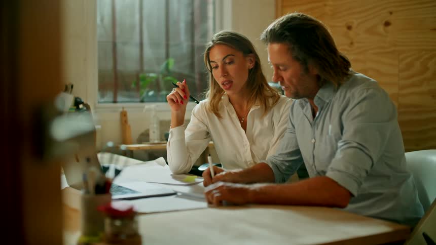A man and woman sit in an office and discuss some work documents they are completing