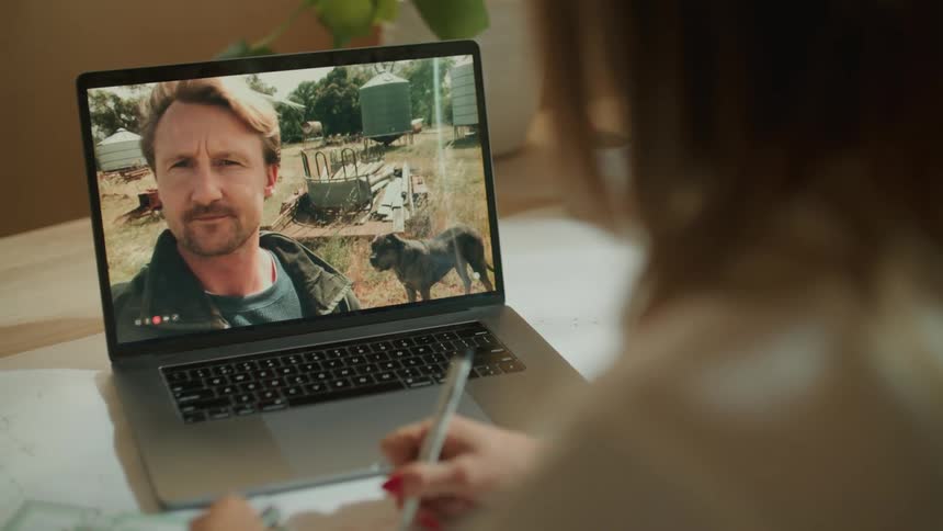 A man talking on a video call to a woman working in an office