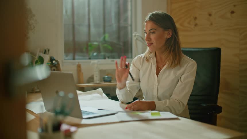 A woman smiles as she talks to someone via video call from her office desk
