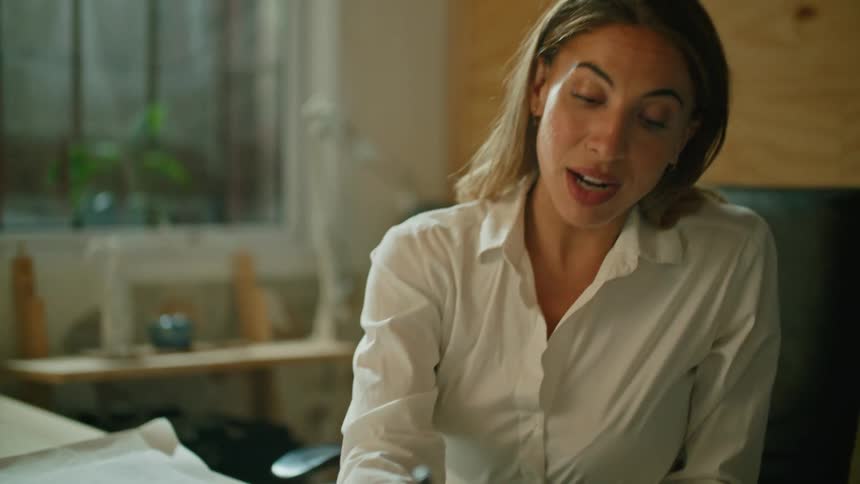 A woman sitting in her office writes on paper as she talks with someone on a laptop