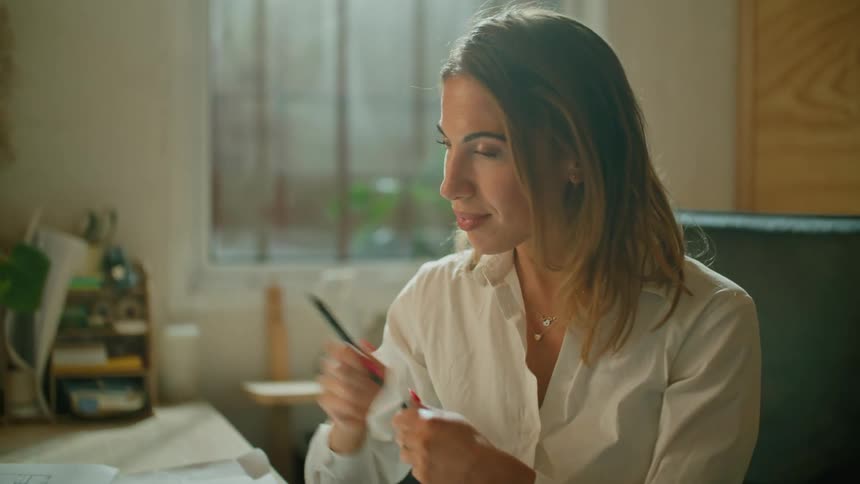 A professional woman talks on a video call and gestures with her pen before signing a document
