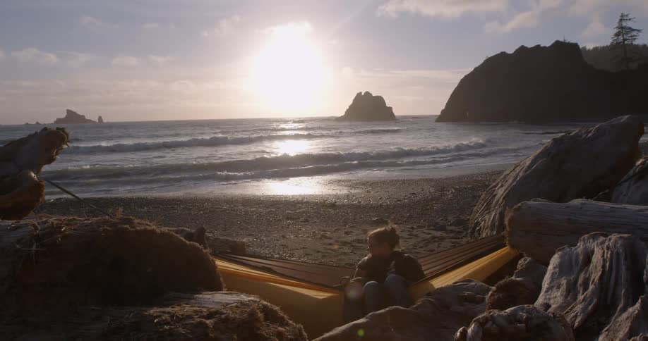 A woman is sitting in a hammock as the sun sets